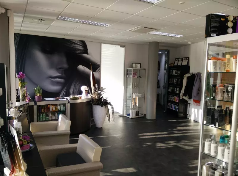 Interieur van de salon met stylingstoelen, een zwart-wit muurschildering, kasten met producten en zonlicht op de vloer